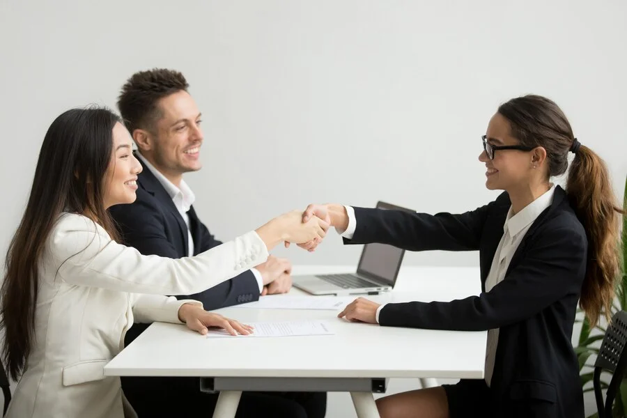 smiling-diverse-businesswomen-shake-hands-group-meeting-deal-concept_1163-4686 – In Hire